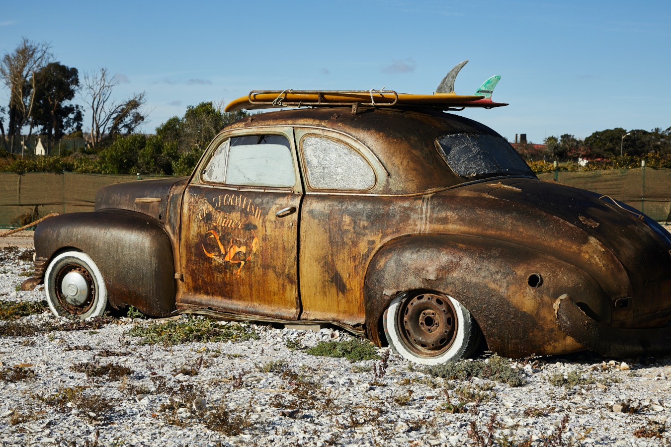 A rusty car sitting on a beach with a surf board